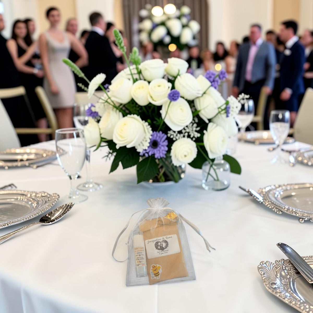Cadeau invité mariage personnalisé présenté sur une table de réception, avec baume à lèvres artisanal à la cire d'abeille, sachet de graines personnalisé et pochon en organza.