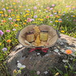 Coffret cadeau artisanal avec miel, bougie naturelle et baume à lèvres posé sur un rocher dans une prairie fleurie, idée cadeau authentique et inspirée de la nature.