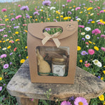 Coffret cadeau artisanal avec miel et bougie naturel, présenté en extérieur dans un décor fleuri, parfait pour un cadeau écologique et authentique.