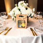 Coffret cadeau invité mariage personnalisé avec pot de miel, baume à lèvres artisanal et bougie en cire d'abeille, présenté sur une table de réception décorée de fleurs blanches.