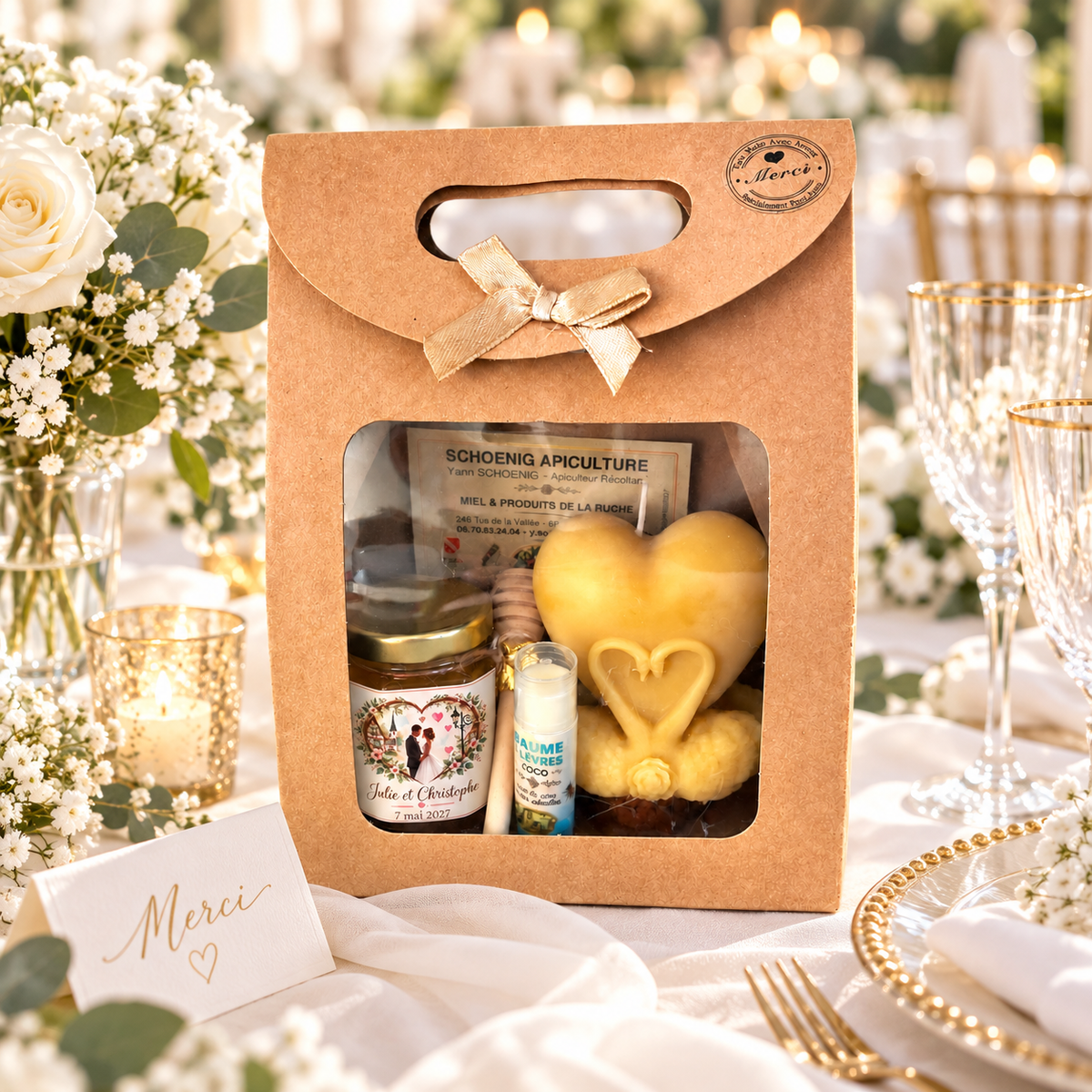 Coffret cadeau invité mariage personnalisé avec pot de miel, bougie cœur aux cygnes et baume à lèvres coco, présenté sur une table de mariage élégante avec fleurs blanches et décoration dorée.