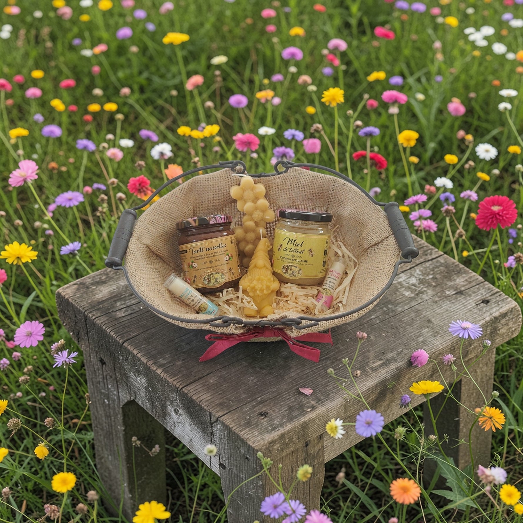 Coffret cadeau naturel avec miel, bougie en cire d’abeille et baume à lèvres posé sur une table en bois dans une prairie fleurie, ambiance champêtre et écologique.