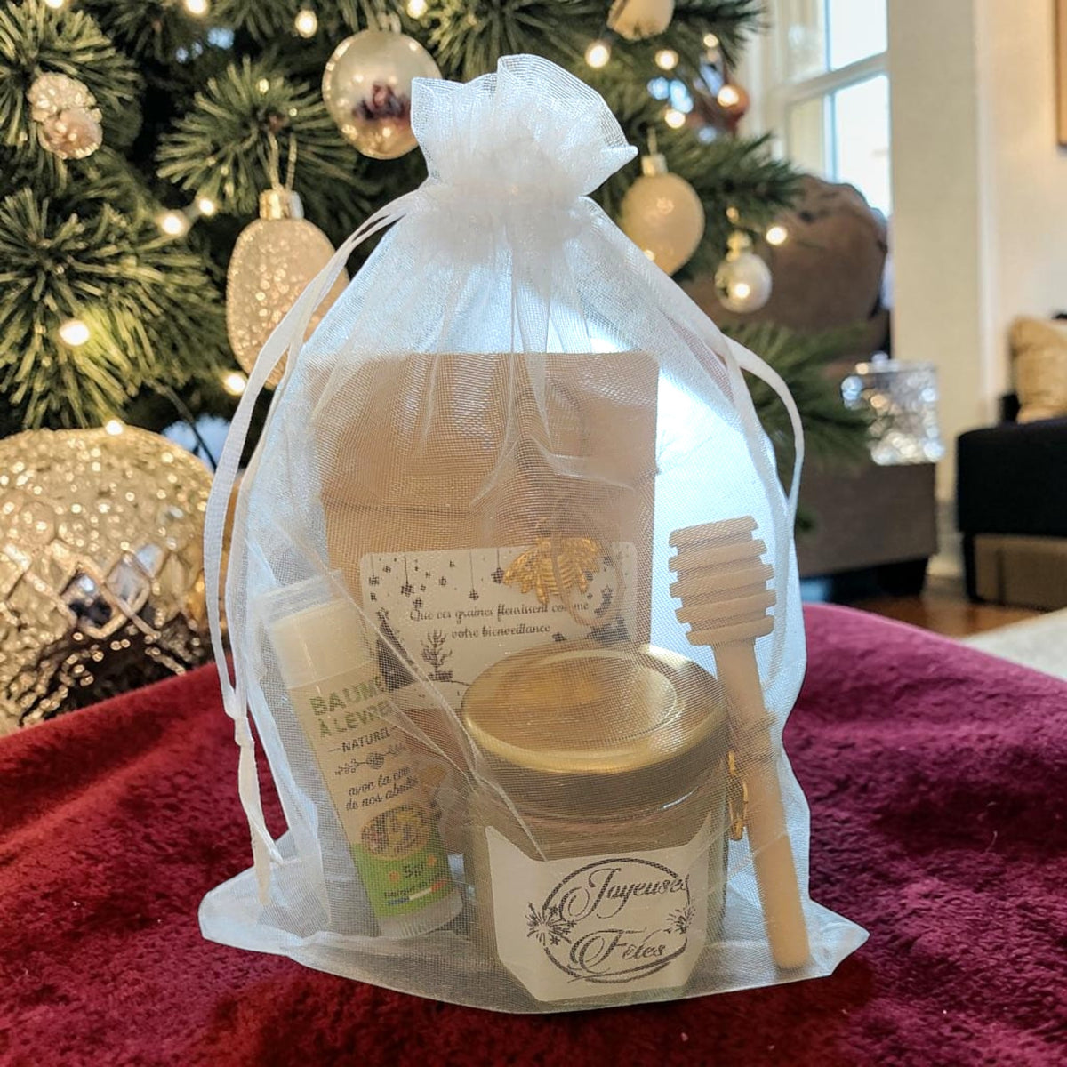 Coffret cadeau de Noël artisanal présenté sous le sapin avec mini pot de miel personnalisé, baume à lèvres à la cire d'abeille, sachet de graines personnalisé et cuillère à miel en bois.