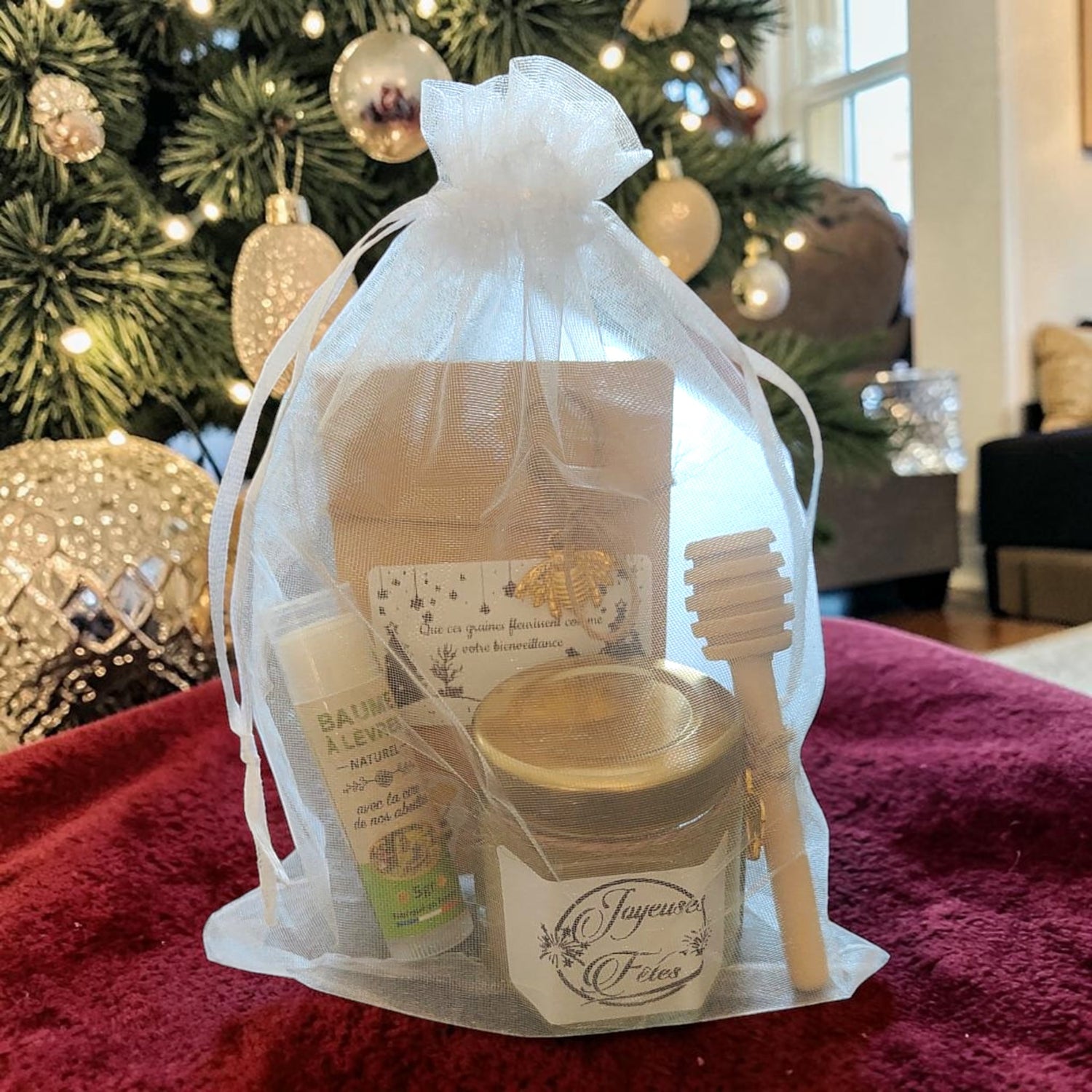 Coffret cadeau de Noël artisanal présenté sous le sapin avec mini pot de miel personnalisé, baume à lèvres à la cire d'abeille, sachet de graines personnalisé et cuillère à miel en bois.