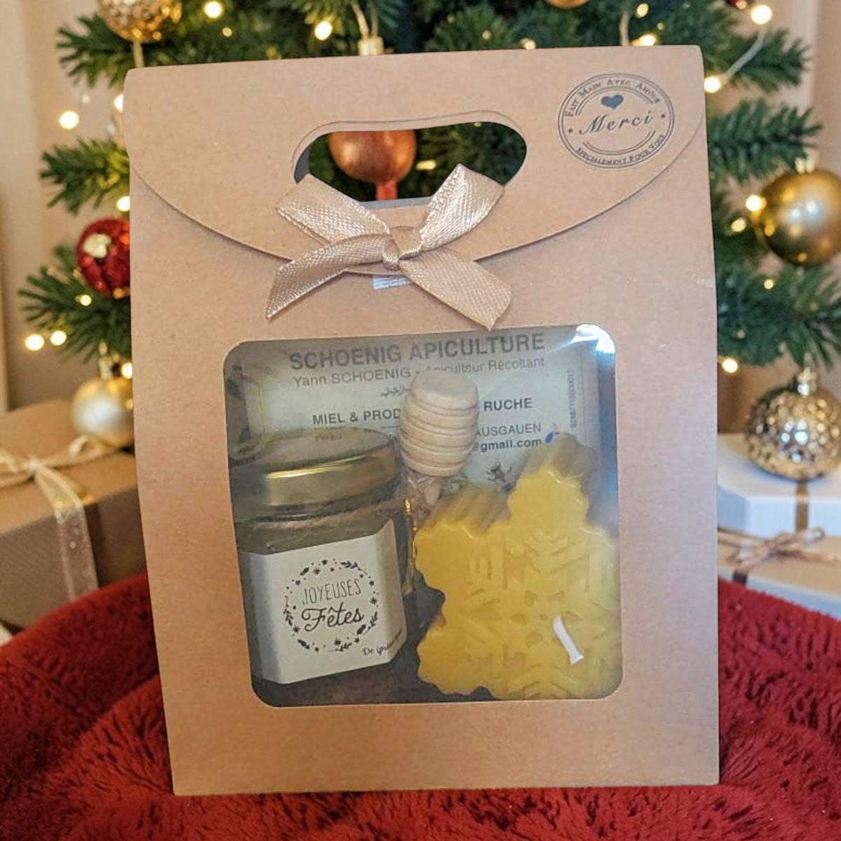 Coffret cadeau de Noël artisanal avec pot de miel de nos ruches, bougie en cire d'abeille en forme de flocon, cuillère à miel en bois et étiquette Joyeuses Fêtes.
