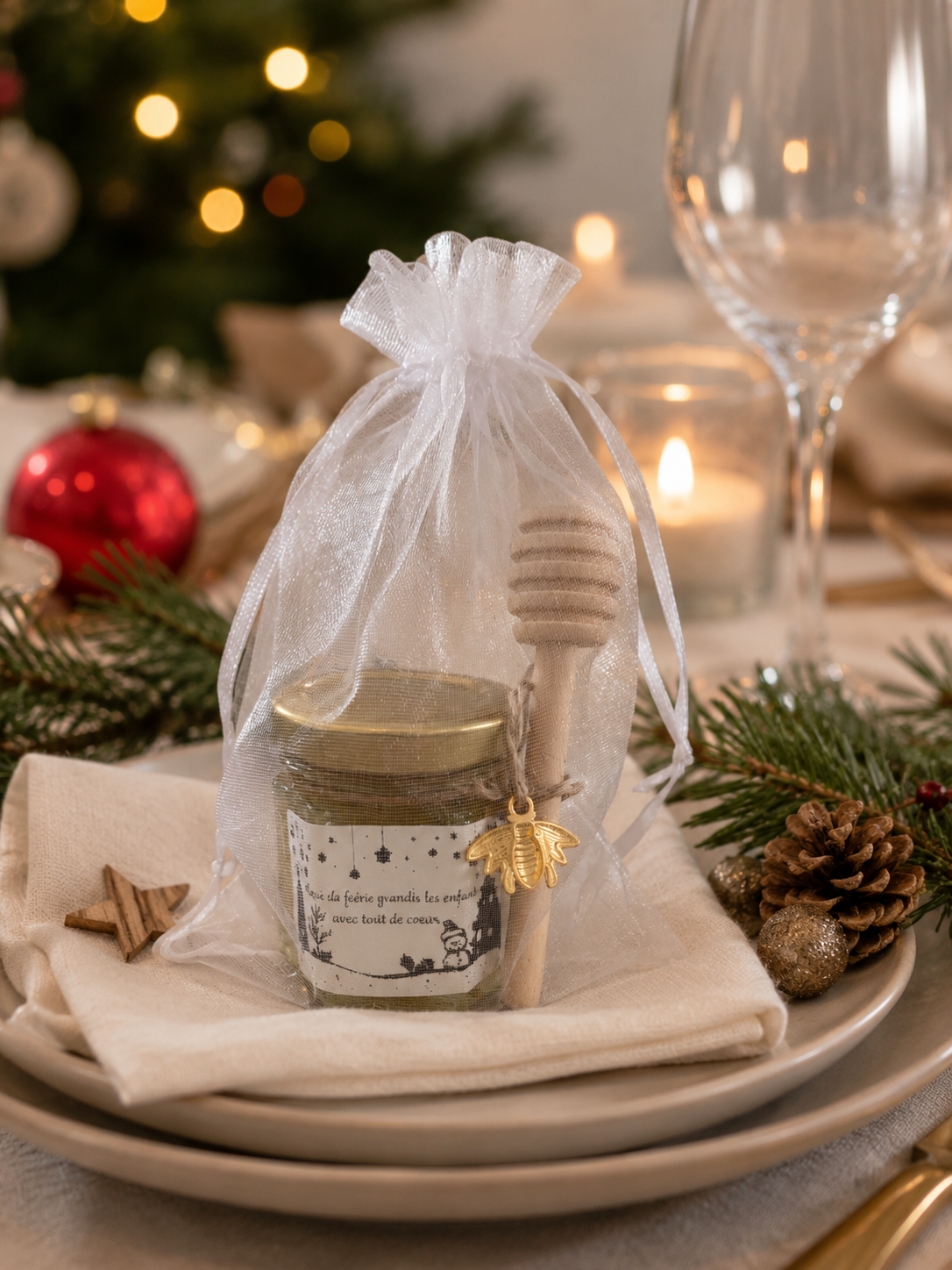 Idée de petit cadeau de Noël pour invités avec pot de miel personnalisé, présenté comme décoration de table de fêtes dans un pochon en organza.